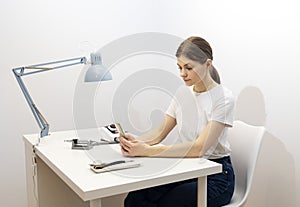 Nail beautician hold gadget, looking at smartphone, sitting at workstation in nail beauty photo