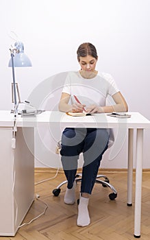 Nail beautician makes notes in notebook with pen, sitting at workstation, table in photo