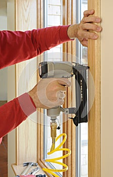 Nail gun being used to install wood trim around wi