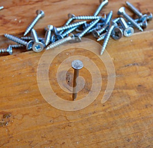Nail hammered in board with fallen screws behind. Soft focus.