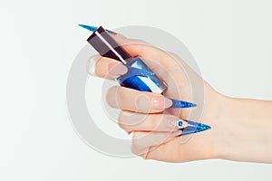 Nail Polish. Art Manicure. Modern style blue Nail Polish. Beauty hands holding blue bottle. Stylish Colorful stiletto Nails