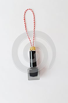 Nail polish as a Christmas tree toy on a red-white string on a white background. Beauty cosmetic New Year concept