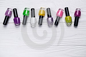 Nail polish bottles in different colors on white wooden background