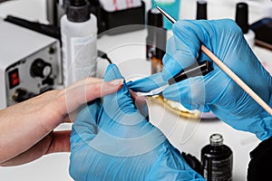 Nail salon. The master in blue protective gloves brushes colorless varnish on the nails