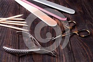 Nail scissors file and clippers to remove the cuticle care products on a dark wooden background