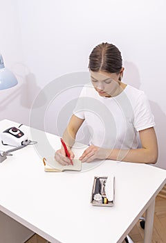 Nail technician makes notes in notebook with pen, sitting at workstation, table in photo