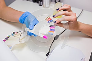 Nail technician shows the color palette of nail services in beauty salon.