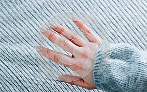 Nails design. Hands with bright silver manicure on gray knitted background.