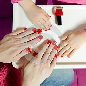 Nails on the hands of mother and daughter painted with red varnish
