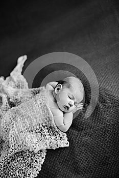 Naked baby covered with shawl sleeps on blanket. Black and white photo