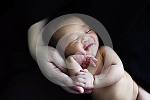 Naked baby newborn have a sweet dream with smile on parent hand.