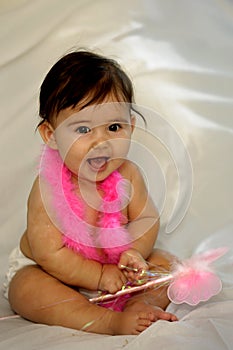 Baby sitting and smiling with pink feathers