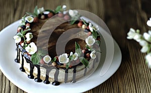 Naked drip cake with chocolate, decorated with strawberries, jasmine flowers and honeysuckle on brown wooden table