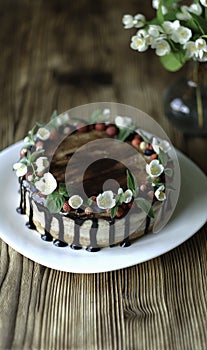 Naked drip cake with chocolate, decorated with strawberries, jasmine flowers and honeysuckle on brown wooden table