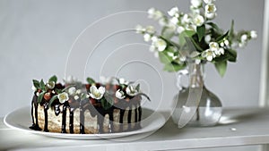 Naked drip cake with chocolate, decorated with strawberries, jasmine flowers and honeysuckle on white wooden table