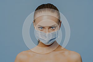 Naked European woman wears disposable medical mask as prevention fromm coronavirus has makeup combed hair poses withh