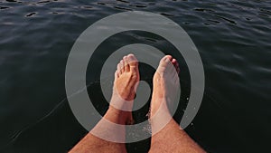 Naked hairy male legs hang from a catamaran. The legs of a man swim towards the waves on a ship. First person of view