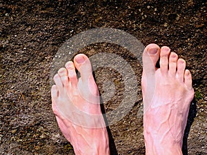 Naked male legs on peak make step. Sandstone rock above valley with tired hikers legs.