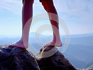 Naked male legs on peak make step. Sandstone rock above valley with tired hikers legs.