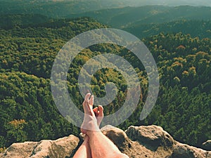 Naked male legs on peak make step. Sandstone rock above valley with tired hikers legs without shoes.