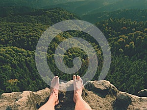 Naked male legs on peak make step. Sandstone rock above valley with tired hikers legs without shoes.