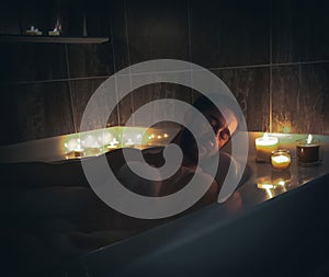 Naked male lying in a bath decorated with candles and foam on him