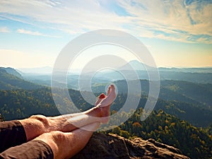 Naked male sweaty legs on peak of rock above valley. The end of trek