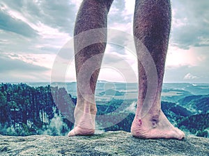 Naked male sweaty legs are resting on peak of rock above valley.