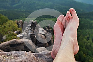 Naked male sweaty long legs on peak of sharp rock above valley.