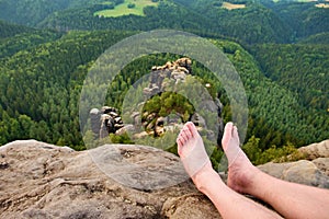 Naked male sweaty long legs on peak of sharp rock above valley.