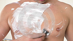 The naked man shaves his chest. A man with white foam for shaving on his chest. Men`s shave body with foam and razor