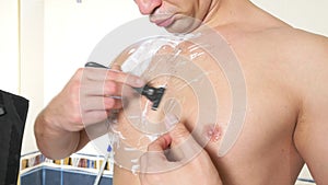 The naked man shaves his chest. A man with white foam for shaving on his chest. Men`s shave body with foam and razor