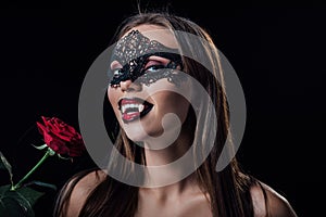 Naked scary vampire girl in masquerade mask showing fangs and holding rose