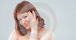 Naked smiling mature woman touches face with hand applying skin care product. Anti-aging skin care concept. Empty space