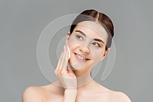 Naked woman cleaning face with cotton pad and smiling isolated on grey