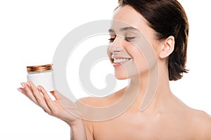 Naked woman looking at container with face cream and smiling isolated on white