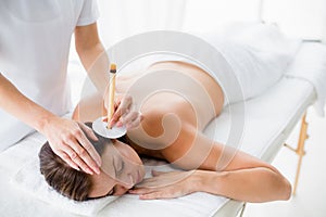 Naked woman receiving ear candle treatment from masseur