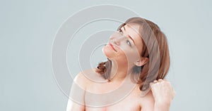 Naked woman smiles looking aside. Pretty mature female touching her long hair with hand, cut out on light gray