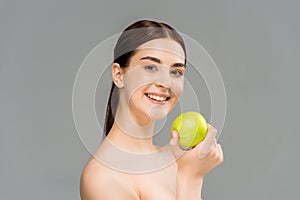 Naked woman smiling while holding green apple isolated on grey