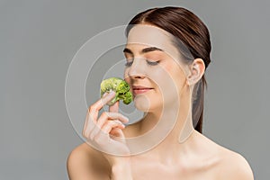 Naked woman smiling while holding green broccoli isolated on grey