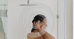 Naked woman standing under the shower washes her hair