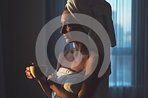 Naked woman with towel on her head and body drinking herbal tea after bath.