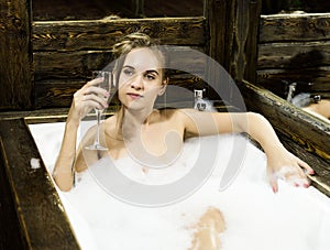 Naked young smiling woman with long hair and straight slim beautiful body lying in white bath tub indoor on wooden