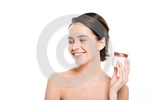 Naked young woman holding container with face cream and smiling isolated on white