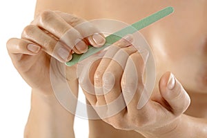 Naked young woman at manicure filing fingernails with nail file in studio