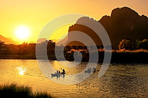 Nam Song River at sunset with silhouetted rock formations and kayakers in Vang Vieng, Laos