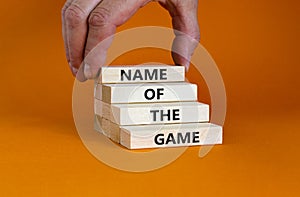Name of the game symbol. Wooden blocks with concept words `Name of the game`. Businessman hand. Beautiful orange background.