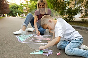 Nanny with cute little boy drawing house with chalks