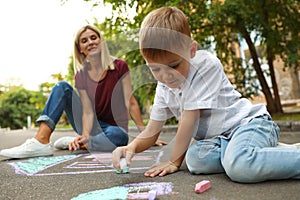 Nanny with cute little boy drawing house with chalks