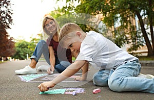 Nanny with cute little boy drawing house with chalks